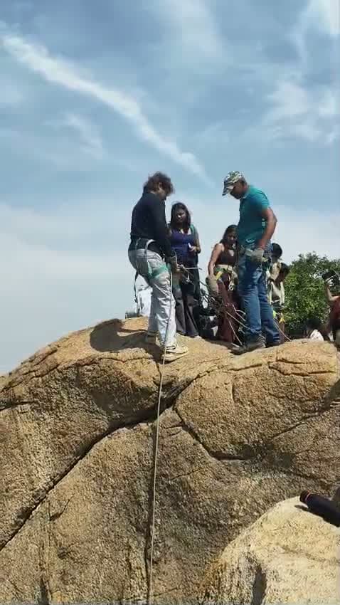 Live action footage of participants preparing and rappelling down steep natural granite rock surface