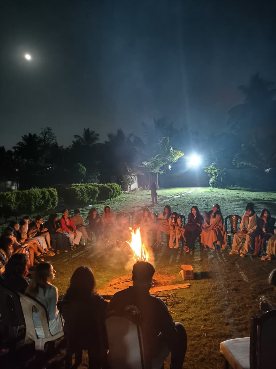 Guests sitting in a full circle around a blazing warm campfire on the resort lawn under moonlit night