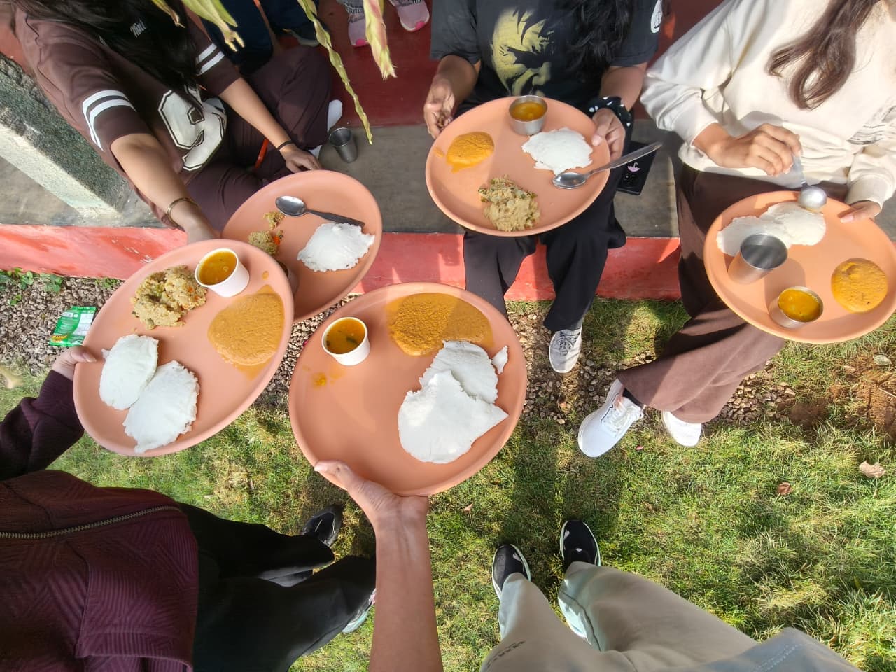 Hot fresh idlis, upma, coconut chutney and sambar served on plates on the green lawn